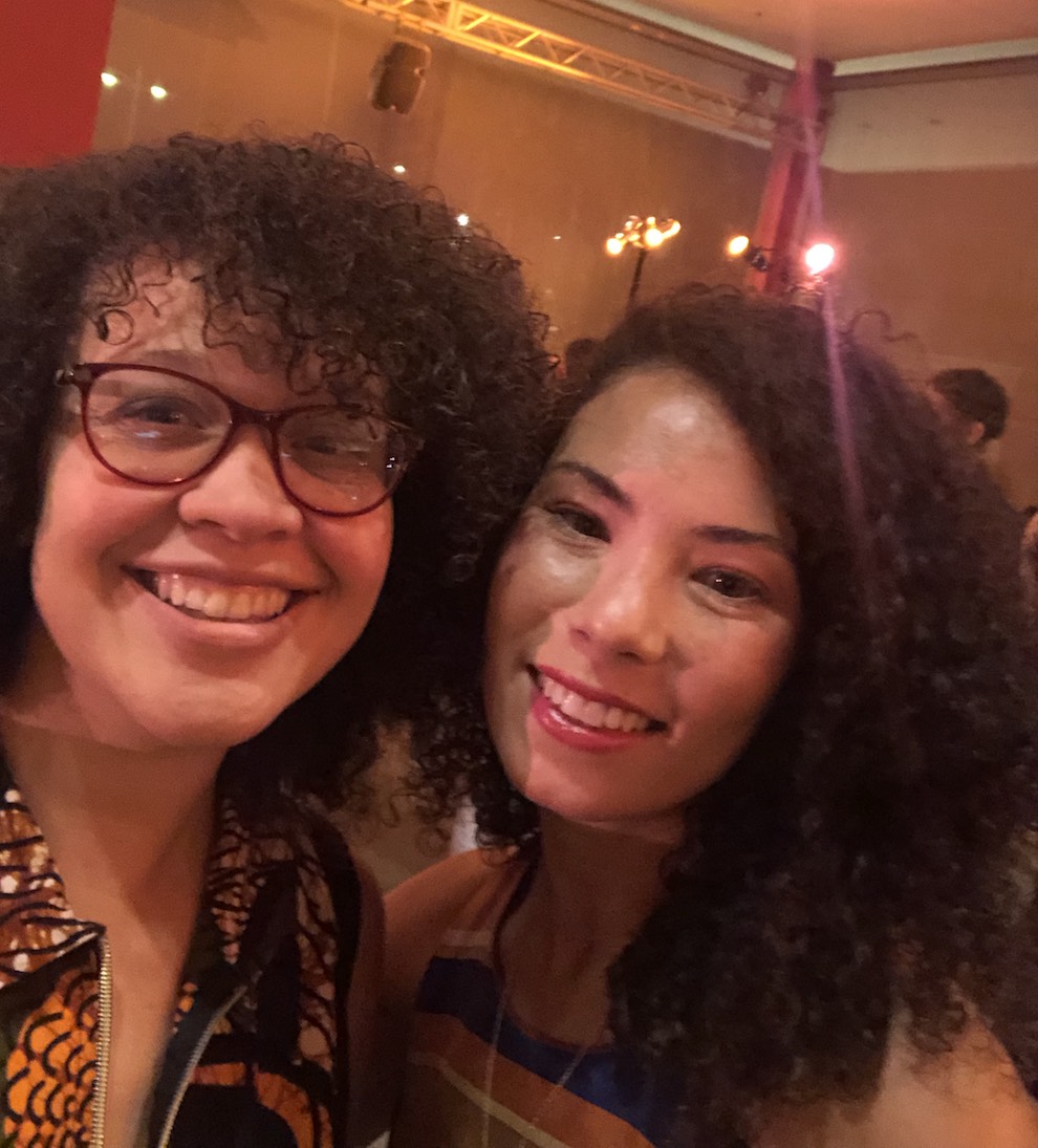 Two women take a selfie. One wears glasses. Both have curly hair